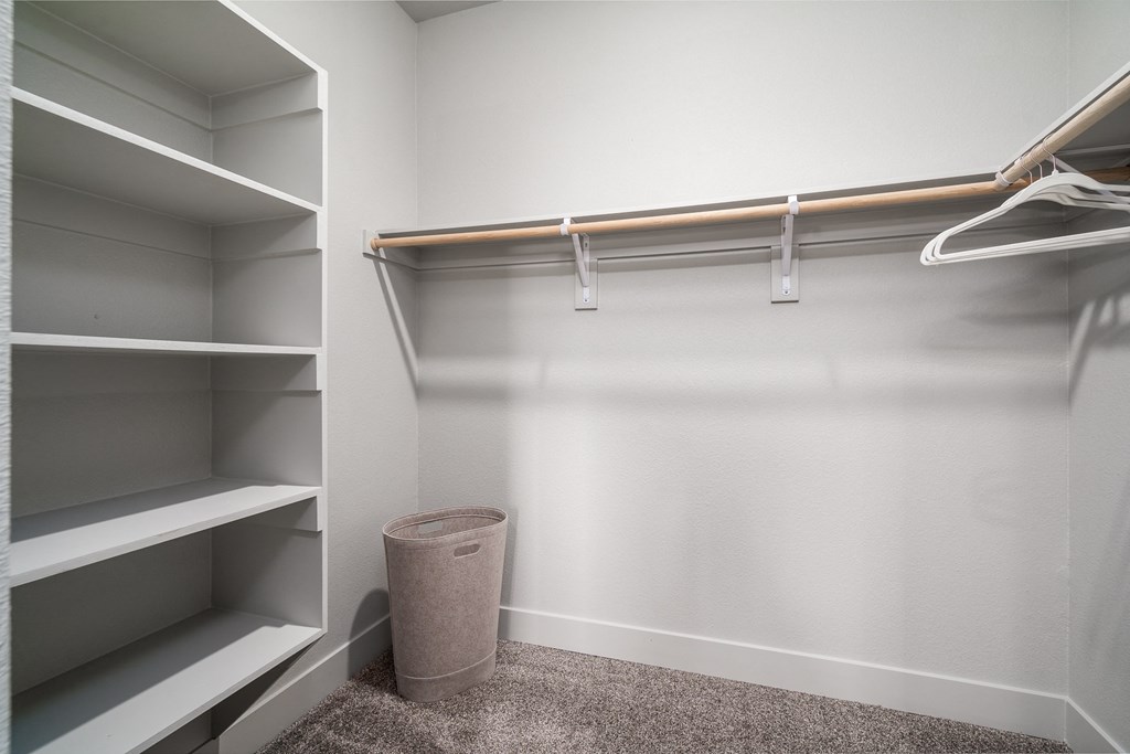 a walk in closet with empty shelves and a trash can