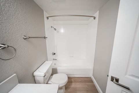 A white toilet sits in a small bathroom with a white tub and shower.
