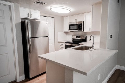 A kitchen with a refrigerator, microwave, oven, and sink.