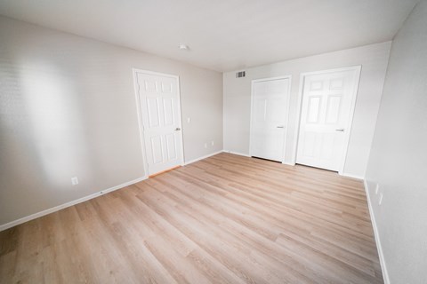 A room with wooden floors and three white doors.