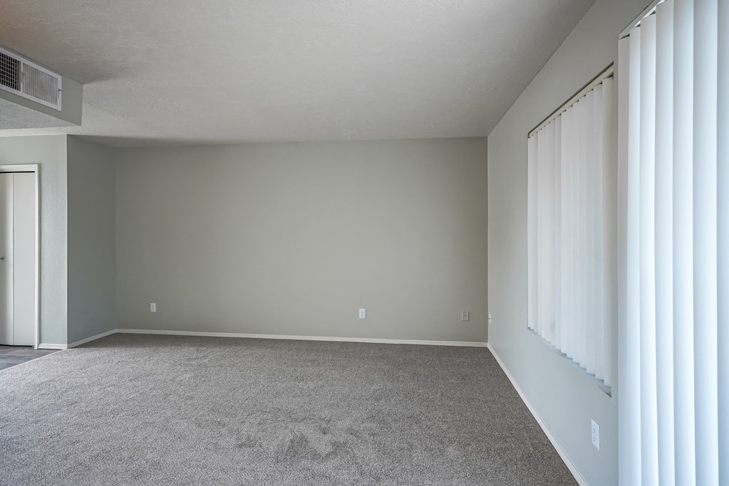 an empty living room with white carpet and a window