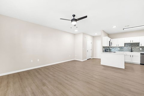 A room with a ceiling fan and a kitchen area in the background.