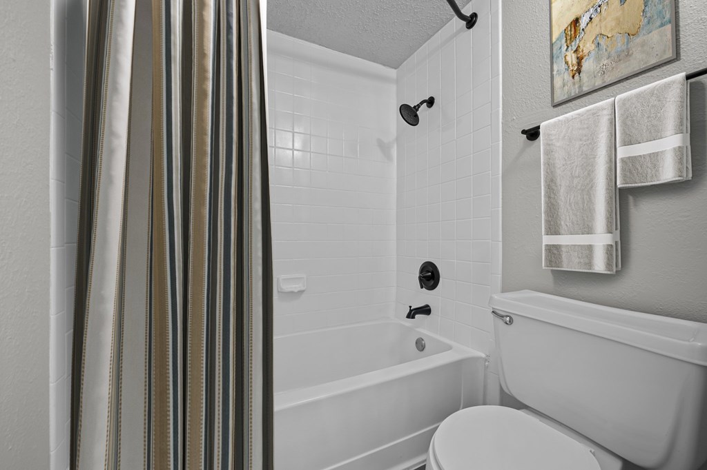 A white bathroom with a toilet, a bathtub, and a shower curtain.