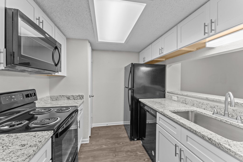A black refrigerator stands in a kitchen with granite countertops and stainless steel appliances.