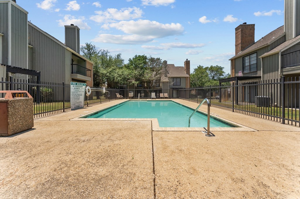 A swimming pool surrounded by a fence and a sandy area.