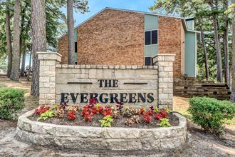 a stone sign that says the evergreens in front of a brick building