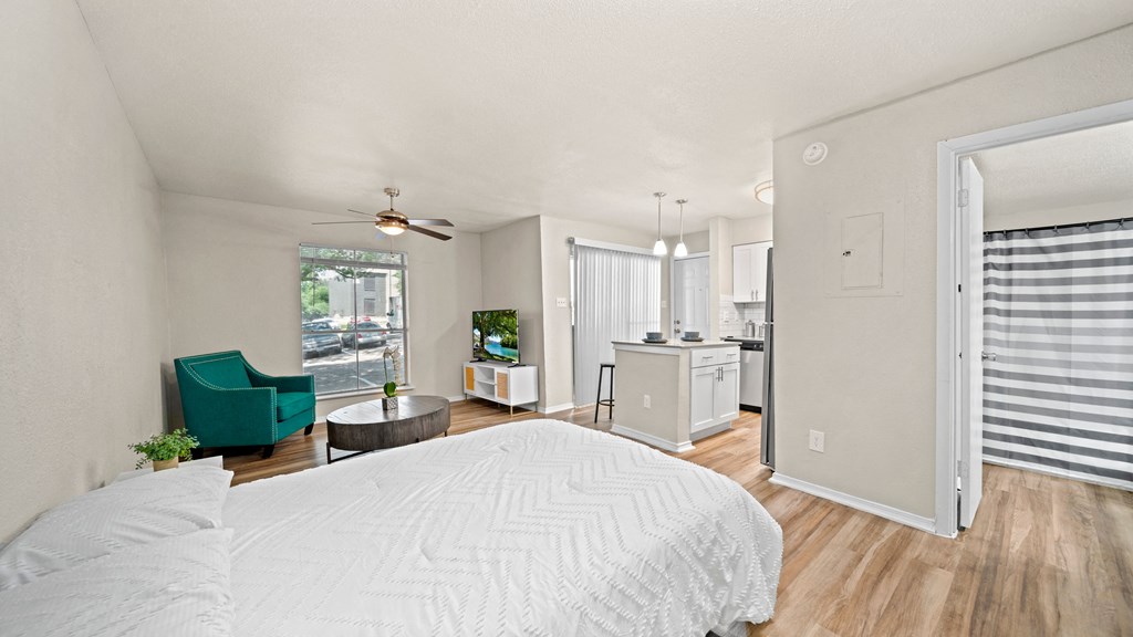 a bedroom with a bed and a chair in a room with a kitchen and a living room