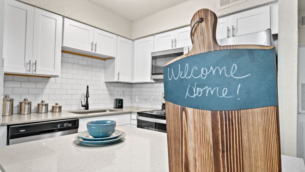 a kitchen with white cabinets and a blue welcome sign