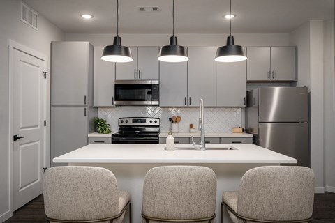 a kitchen with white cabinets and a white island with three chairs