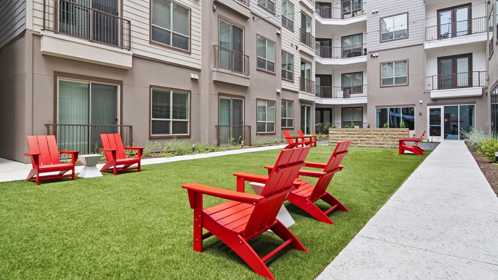 red adirondack chairs on a grassy area with an apartment building in the background