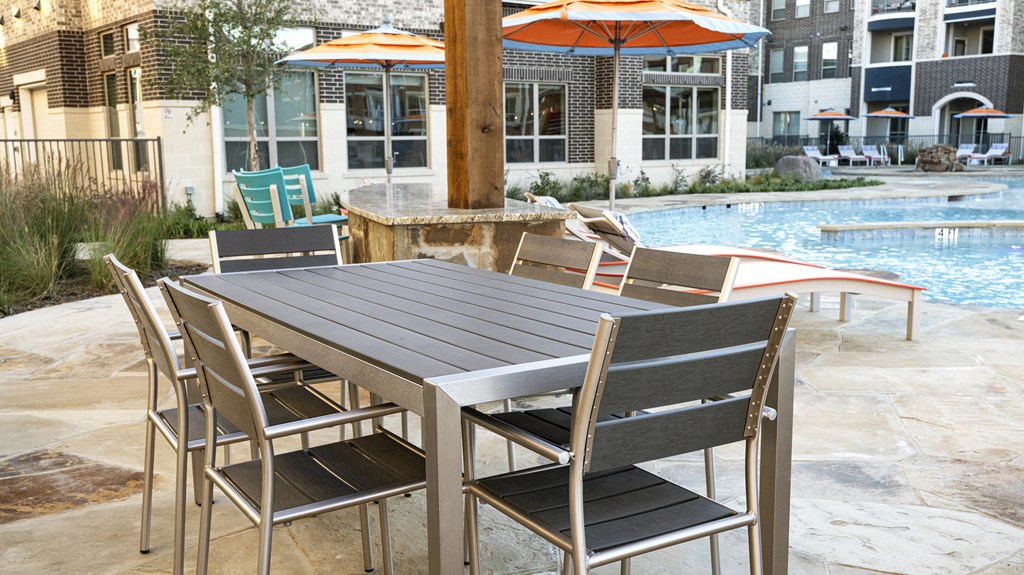 a dining table with chairs and umbrellas next to a pool