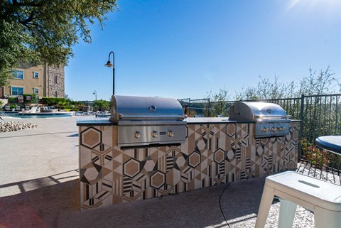 A large outdoor kitchen with a patterned tile backsplash and a grill.