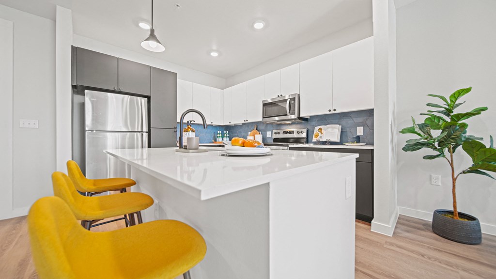a kitchen with white cabinets and a white island with yellow chairs