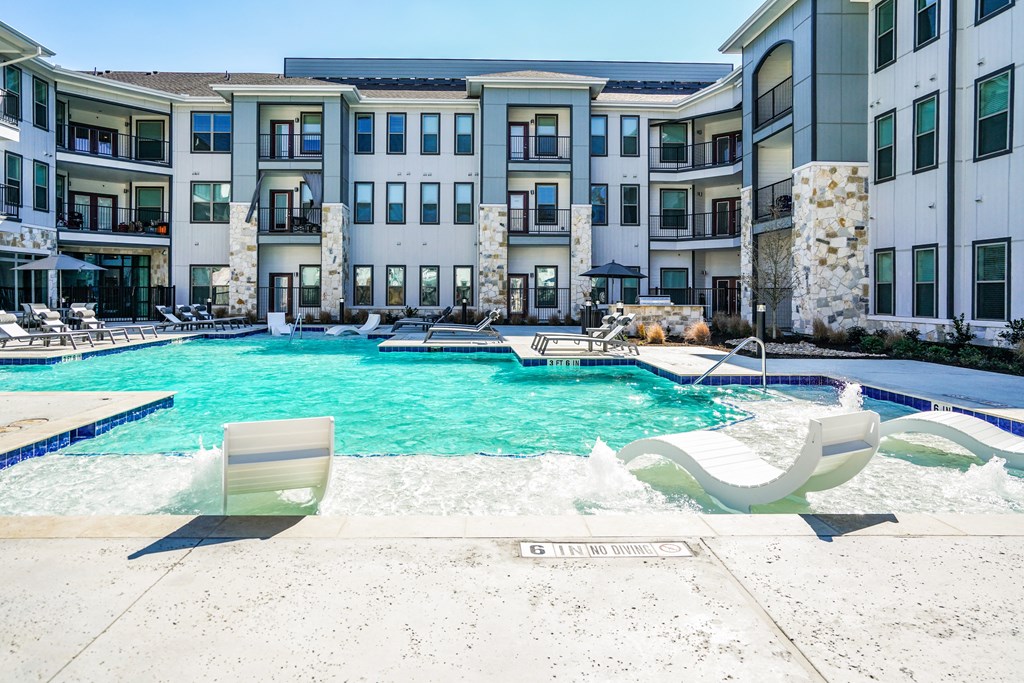an apartment pool with chairs and an apartment building in the background