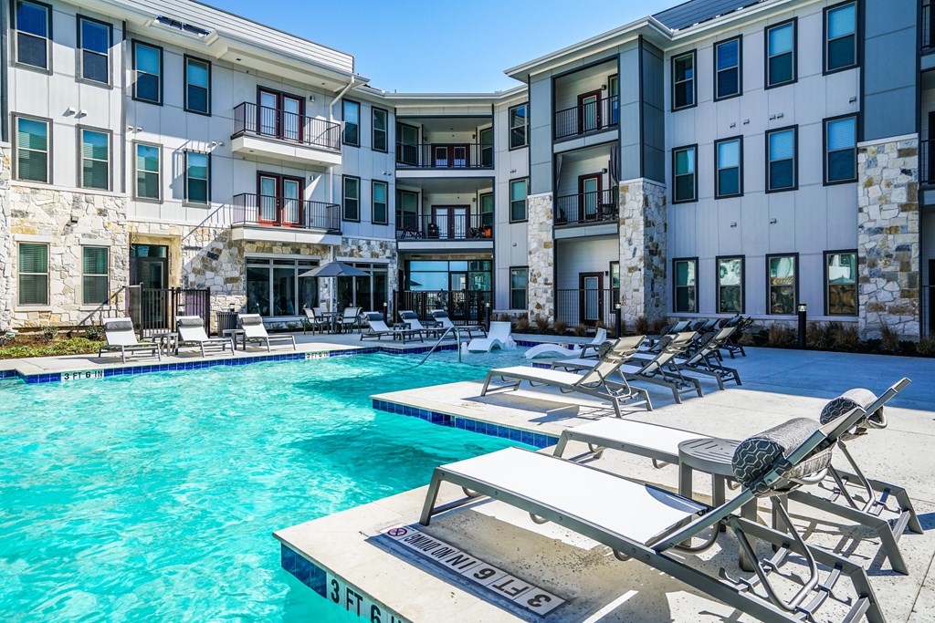 a swimming pool with lounge chairs in front of an apartment building