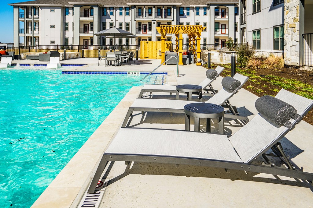 a pool with lounge chairs and tables next to a swimming pool