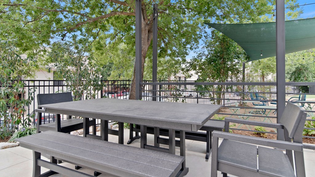 a picnic table and benches on a patio with trees and a building in the background