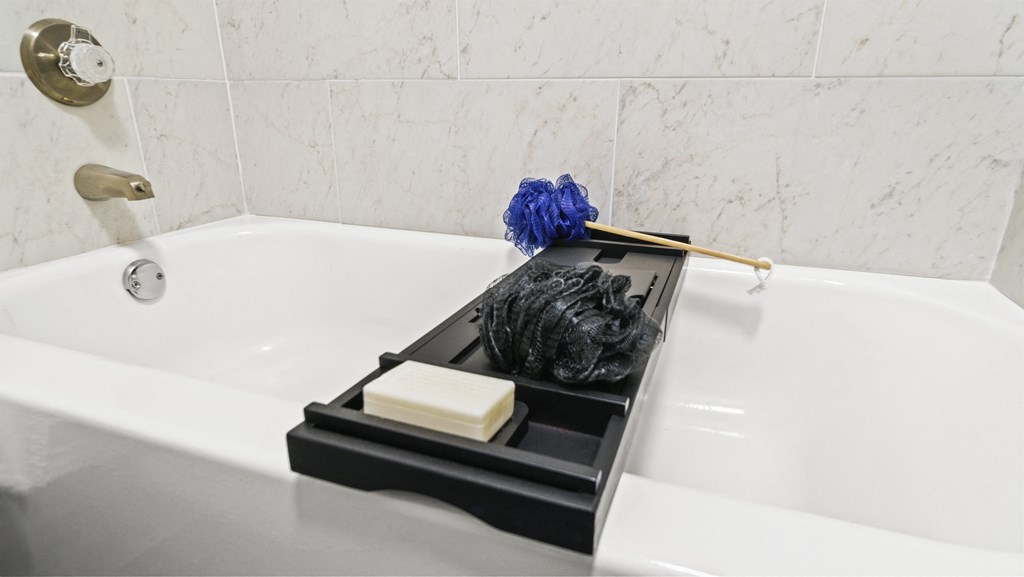 a bathtub with a black plastic tray with a brush on top of it and a white