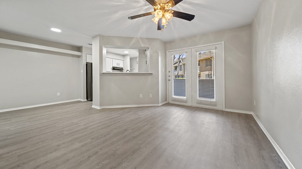 an empty living room with a ceiling fan and french doors to the kitchen