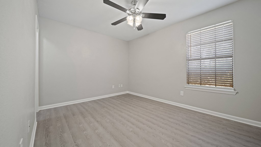 an empty bedroom with a ceiling fan and a window
