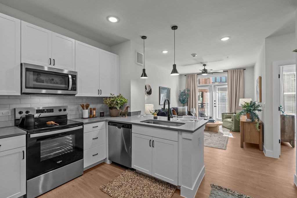 A modern kitchen with a stainless steel oven and microwave, a sink with a faucet, and a rug on the floor.