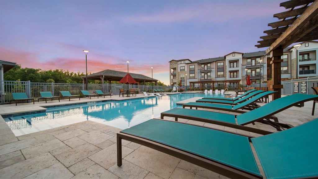a swimming pool with blue chaise lounge chairs and a building in the background