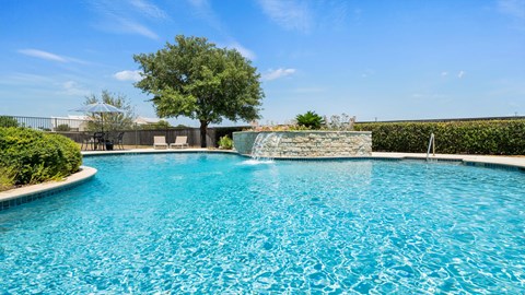 A pool with a waterfall and a tree in the background.