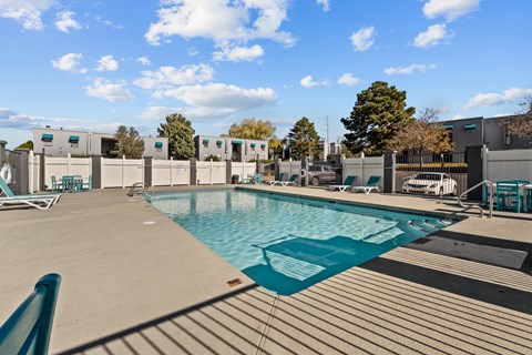 a swimming pool at an apartment complex with chairs and a privacy fence
