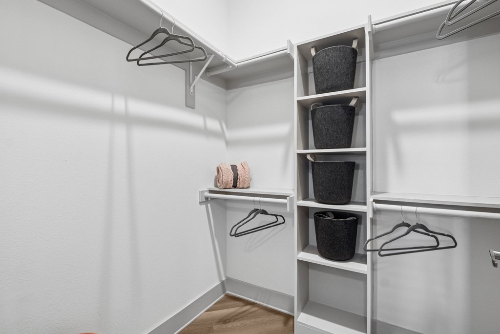 A white closet with clothes hanging and baskets on shelves.