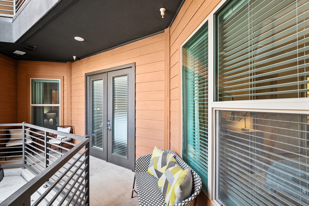 A chair with a yellow and grey blanket is in front of a window with blinds.