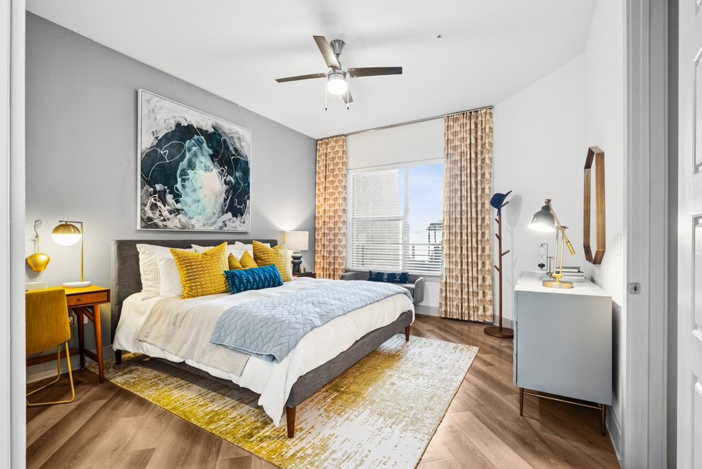 A bedroom with a bed, a desk, and a ceiling fan.
