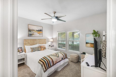 A bedroom with a bed, a ceiling fan, and a television.