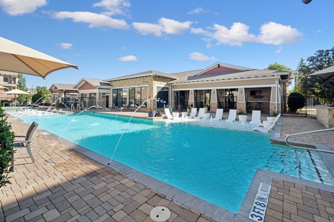 A large outdoor swimming pool with a sun lounger and a building in the background.