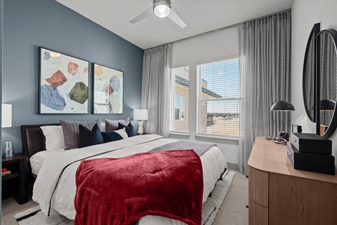 A bedroom with a bed covered in a red blanket and a ceiling fan above it.