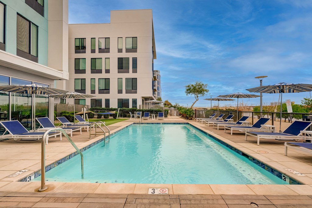 A large swimming pool with lounge chairs and umbrellas in front of a modern building.