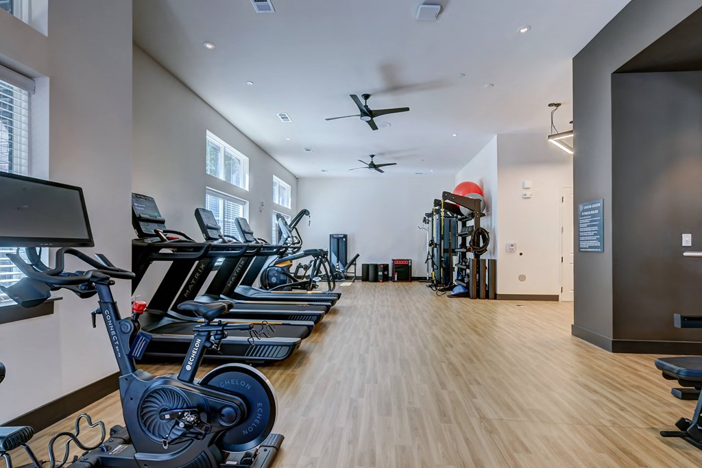 a gym with cardio machines and a ceiling fan
