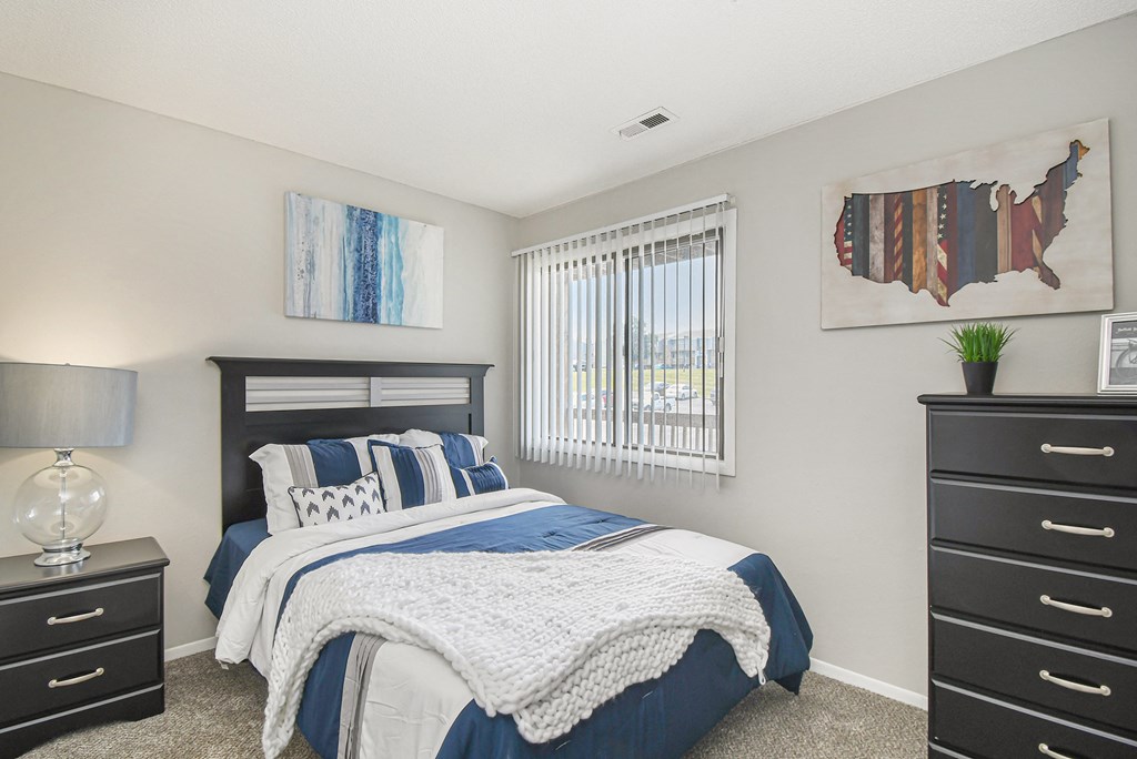 a bedroom with a bed and two dressers and a window