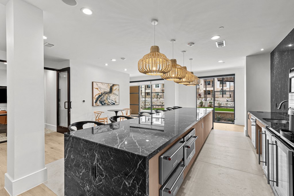 A modern kitchen with a marble island and pendant lights.