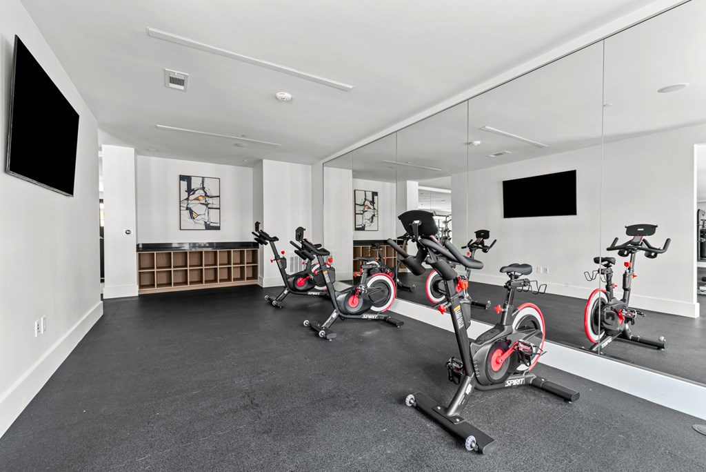 A room with a row of stationary bikes and a television.