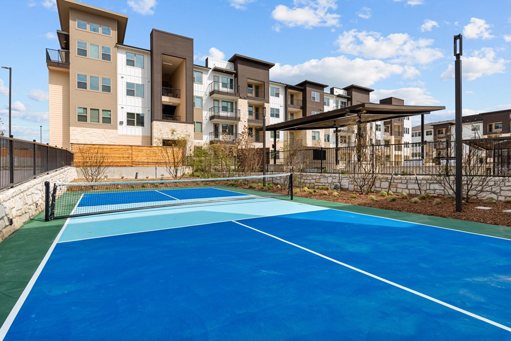 A tennis court is surrounded by apartment buildings.