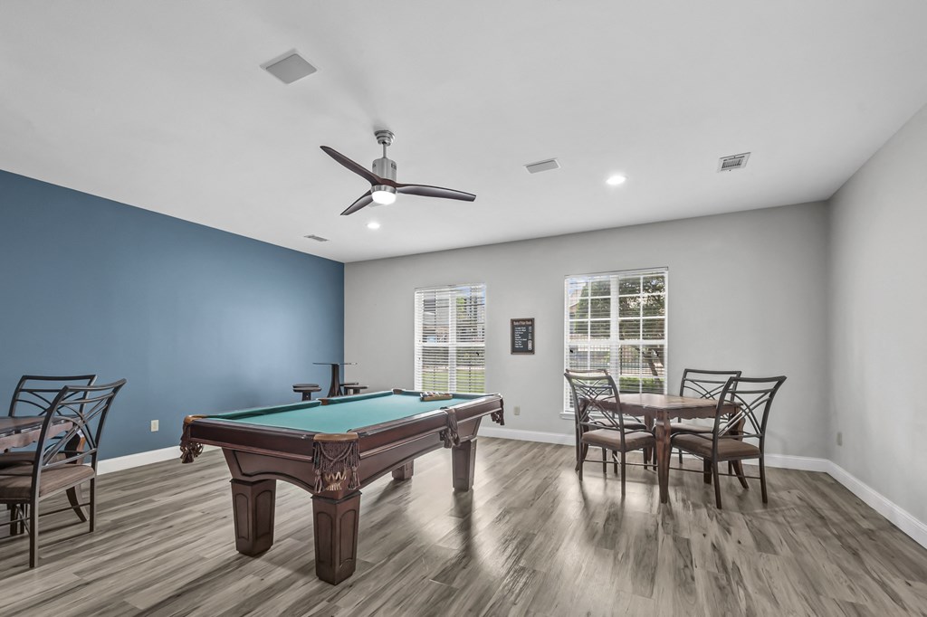 A pool table is in the middle of a room with a ceiling fan.