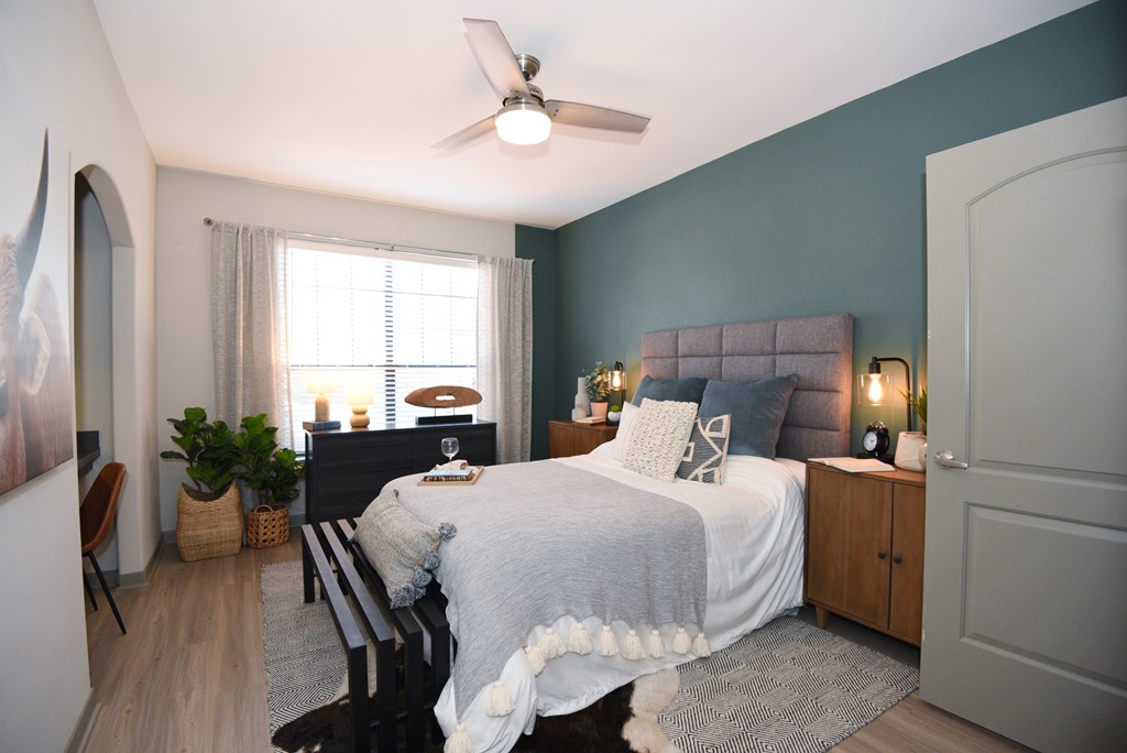A bedroom with a bed, a chair, a ceiling fan, and a window.