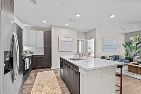 A modern kitchen with a refrigerator on the left and a dining area with a blue couch.