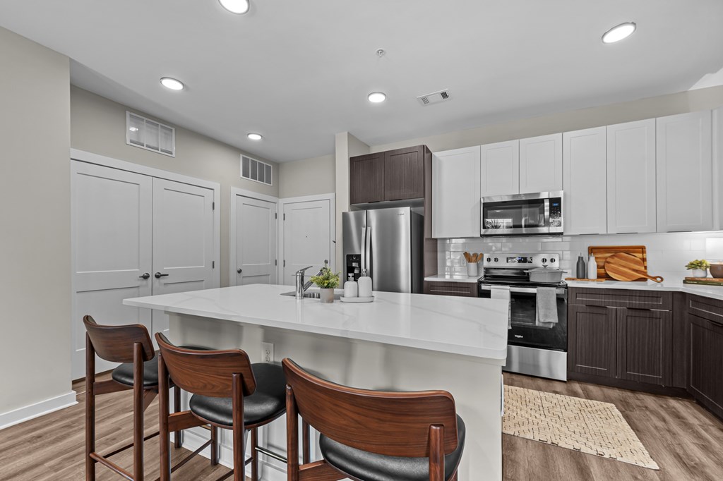 A kitchen with a white island and brown chairs.