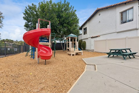 A playground with a red slide and a green picnic table.