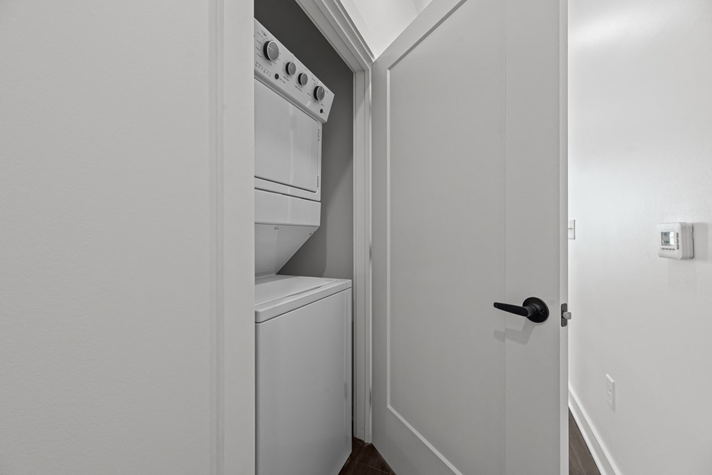 A white door with a black handle is open to a small kitchen with a white oven and cabinet.