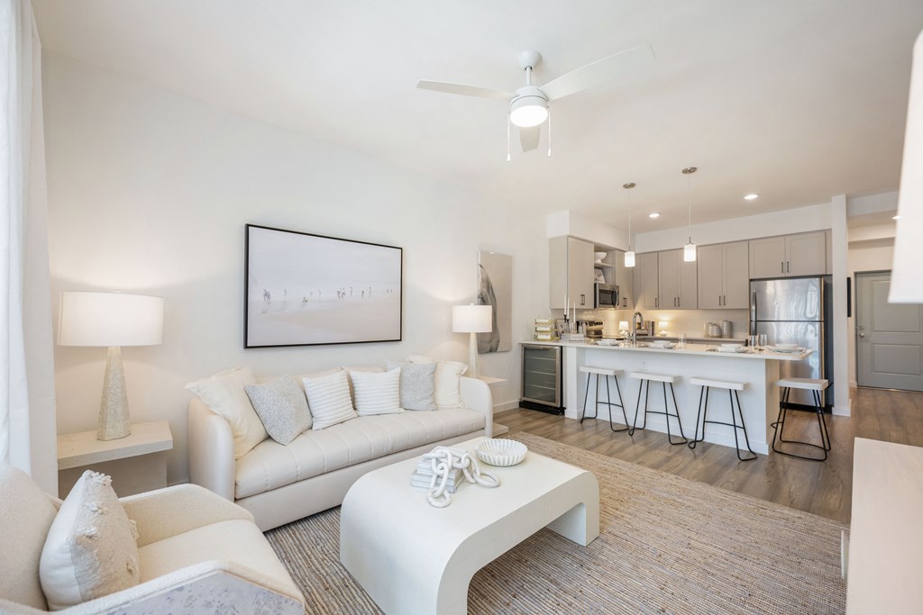a living room with a white couch and coffee table and a kitchen in the background