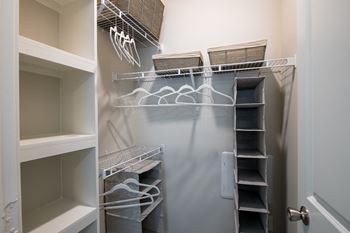 a walk in closet with white shelves and a gray wall