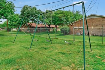 A swing set in a grassy area with a fence and a building in the background.