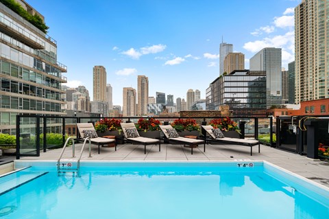 A swimming pool on a balcony with lounge chairs and a city skyline in the background.